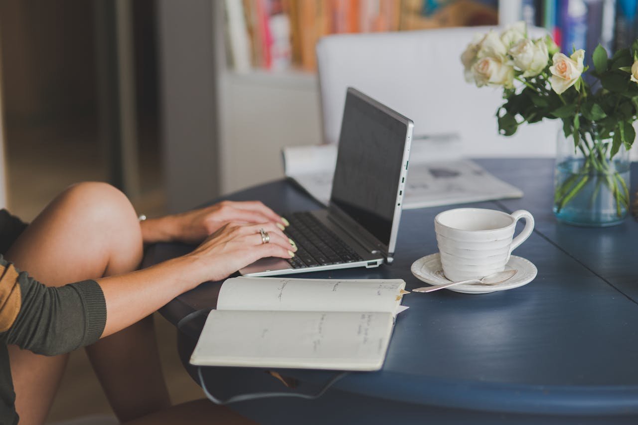 Person typing on a laptop with a notebook and coffee, preparing for a polygraph test